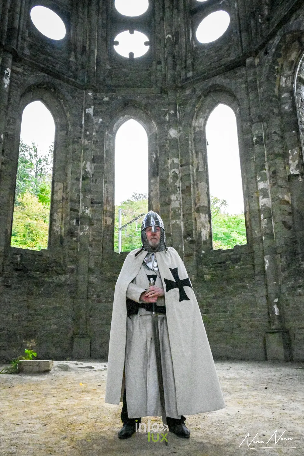 Un chevalier en cape blanche à croix noire debout dans le chœur de l’abbatiale, sous les hautes fenêtres