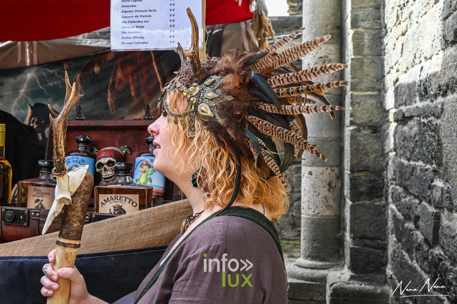 Une femme coiffée de plumes, de profil, devant un stand du marché