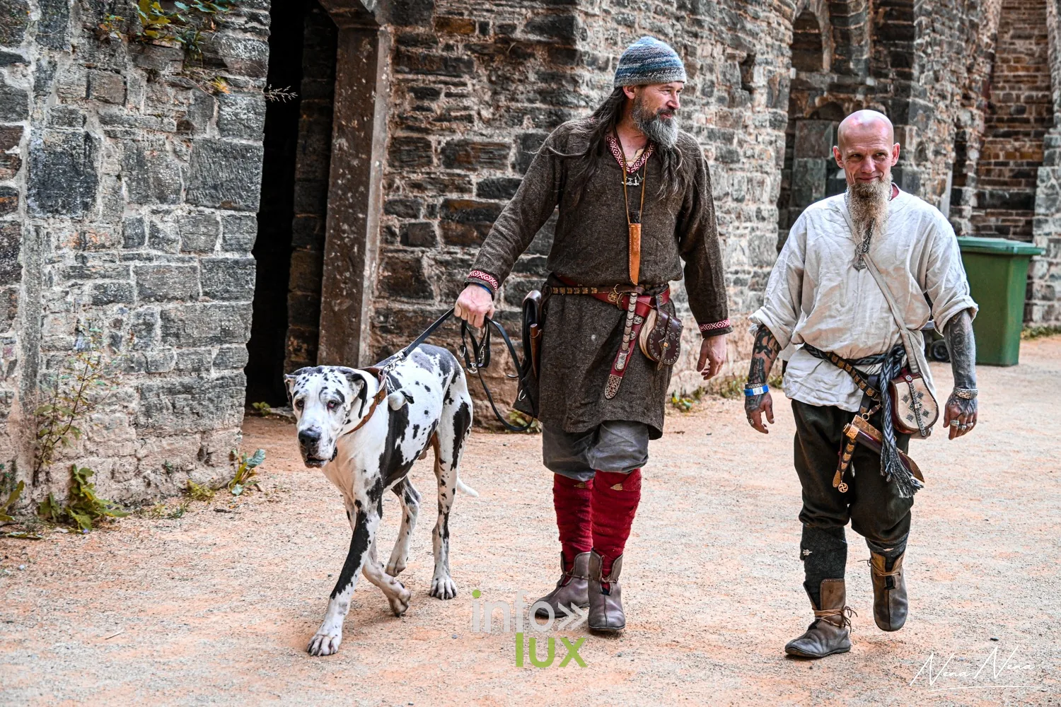 Deux hommes en costume médiéval marchent avec un dalmatien dans la cour de l’abbaye