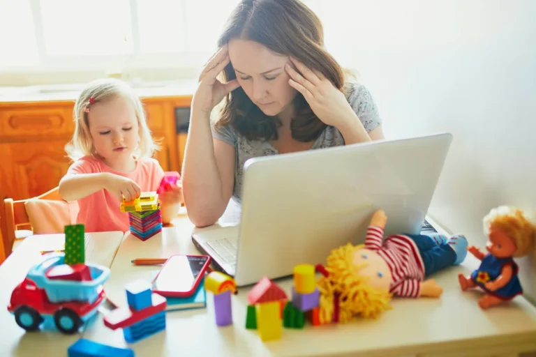 Une maman devant son ordinateur, la tête entre les mains, pendant que sa fille joue à côté d’elle