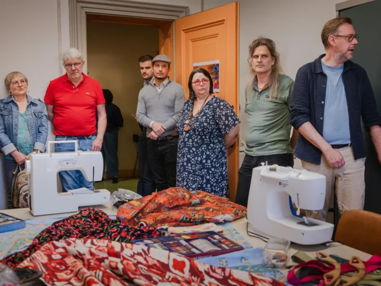 Machines à coudre et tissus sur une table du Repar’Couture, entourés de visiteurs, à la MJC d’Audun-le-Tiche