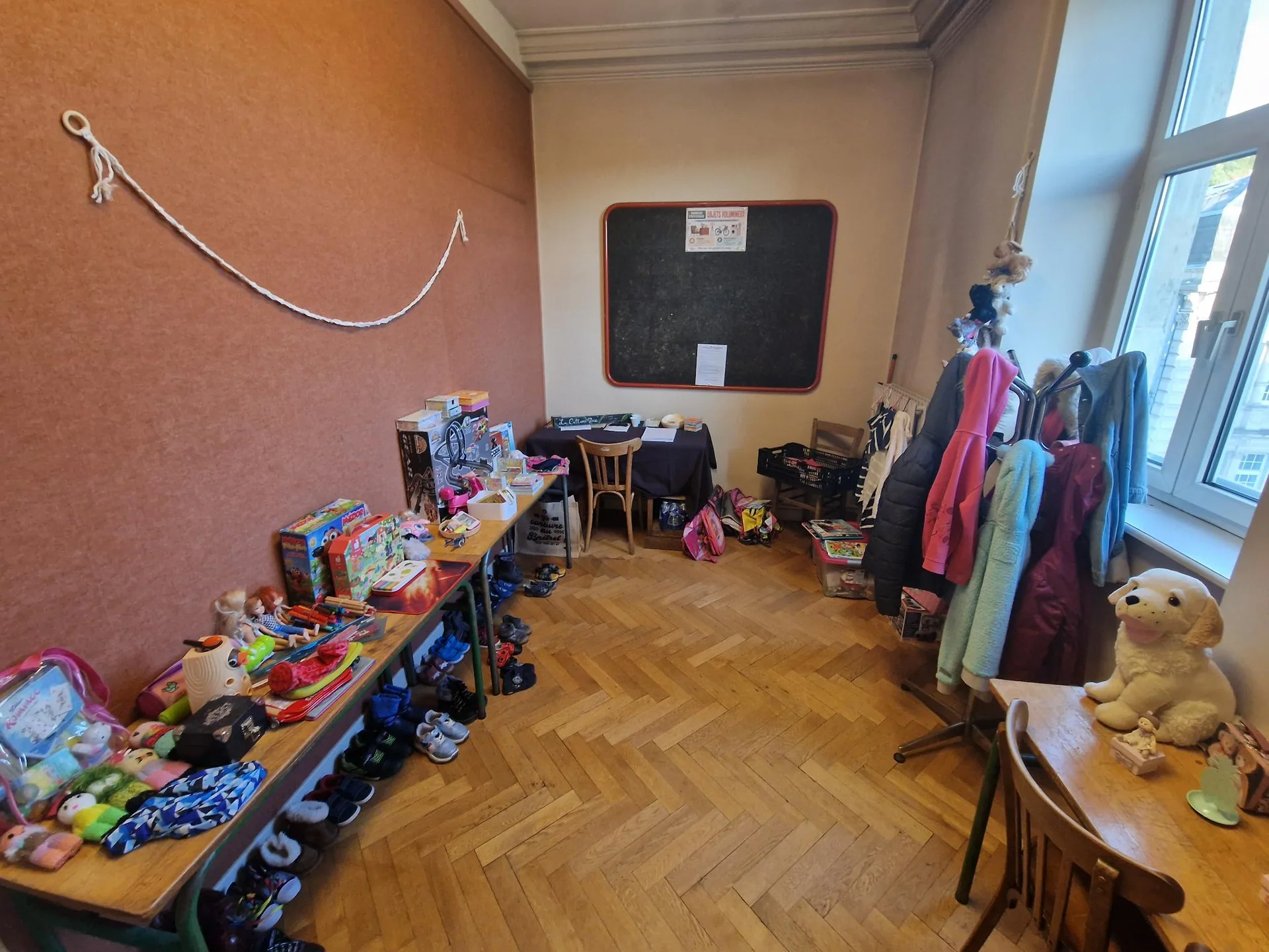 Salle de la donnerie Culture Box avec tables de jouets, portants de vêtements et tableau noir