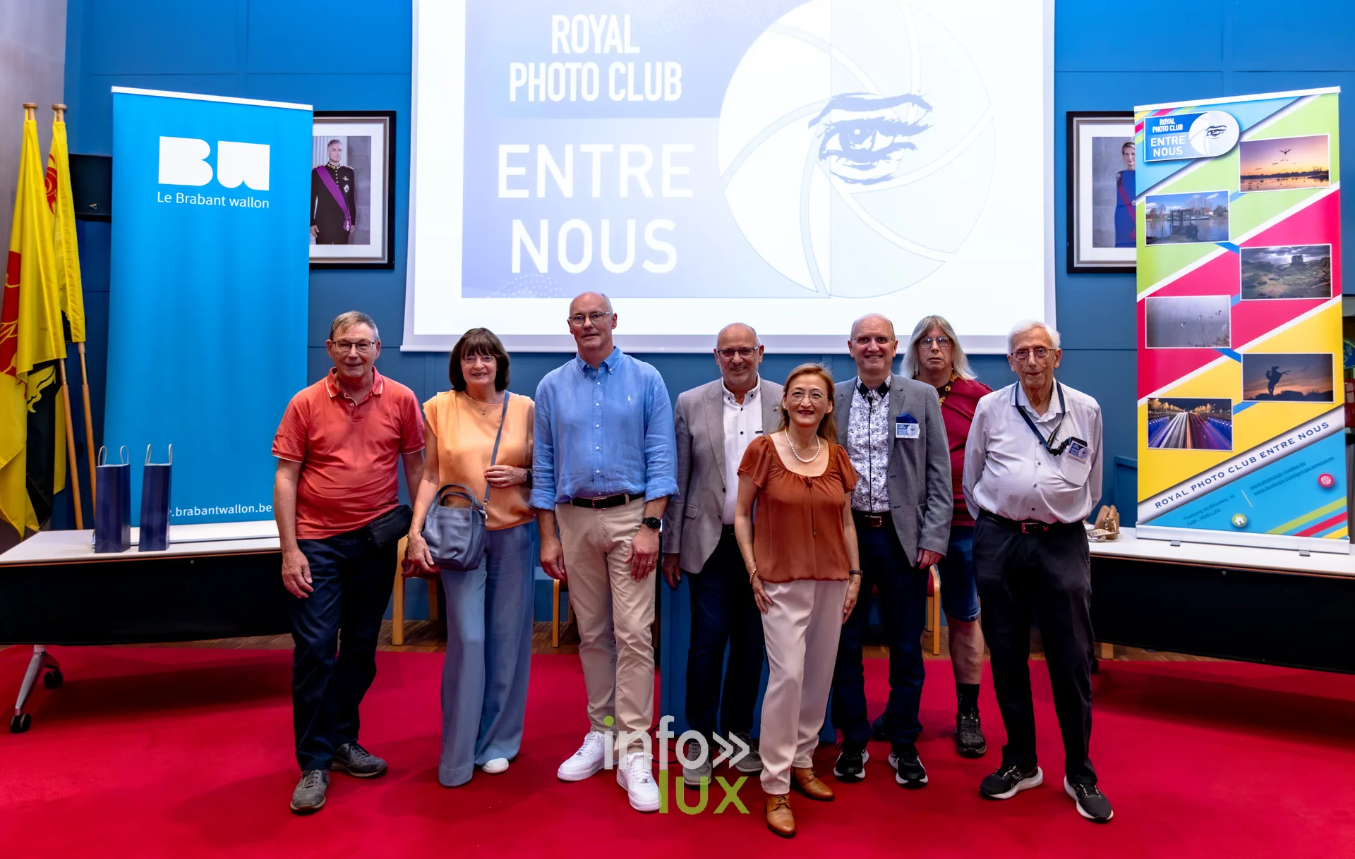 Photo de groupe des membres du Royal Photo Club Entre Nous devant le visuel du club à l’Hôtel de Ville de Nivelles
