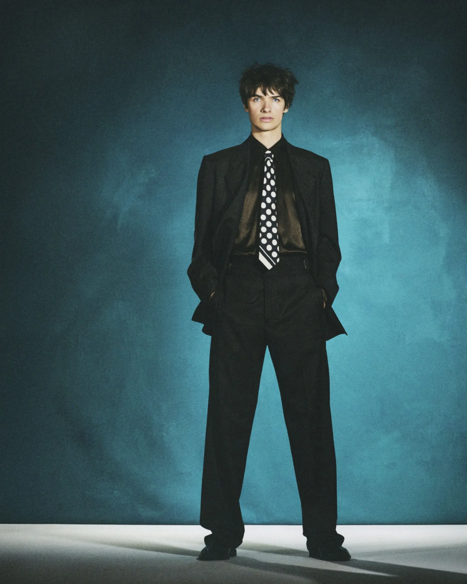 Pierre de Maere en costume sombre, photo en pied sur fond bleu