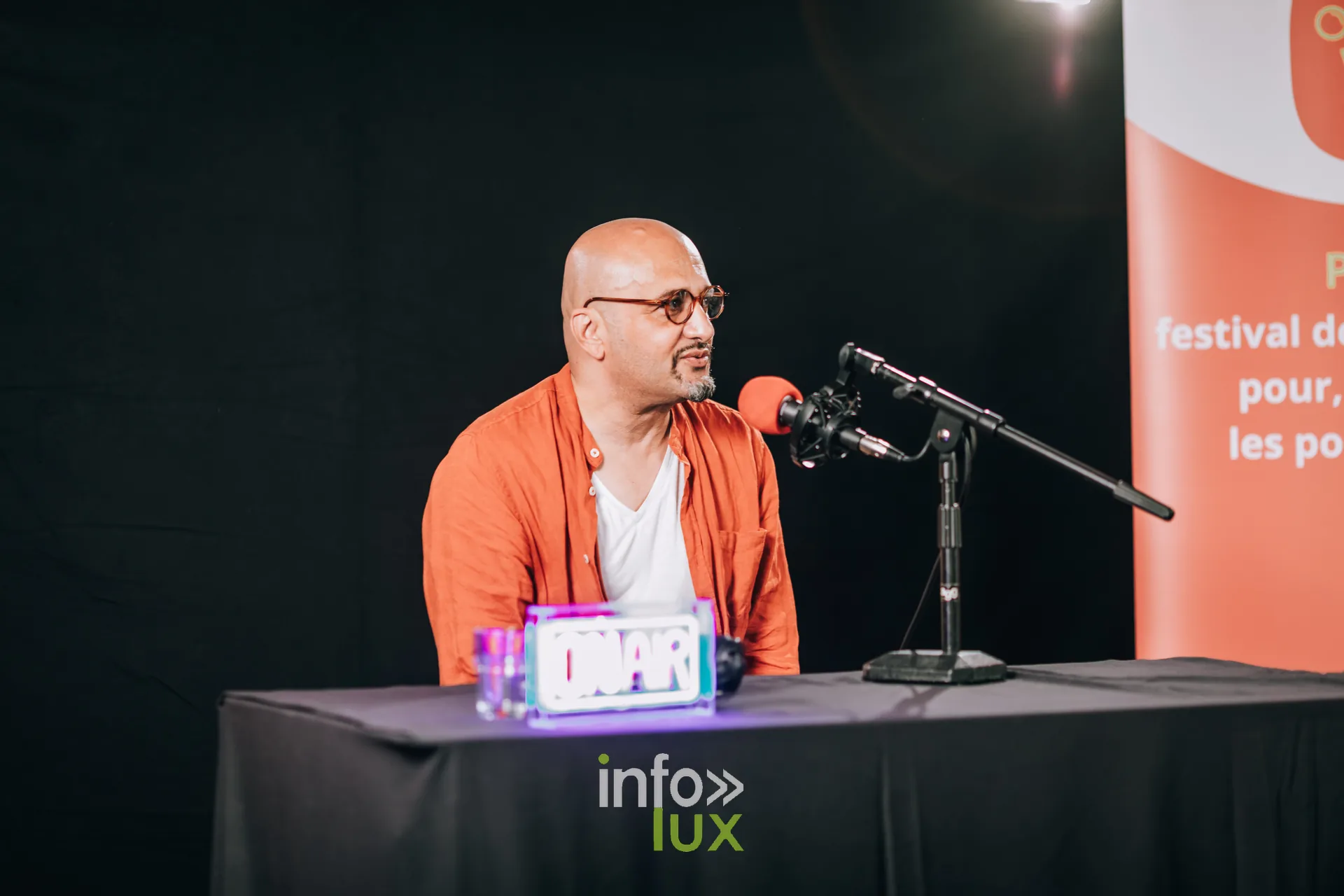 Animateur en chemise orange au micro sur la scene du festival PodBXL 2026