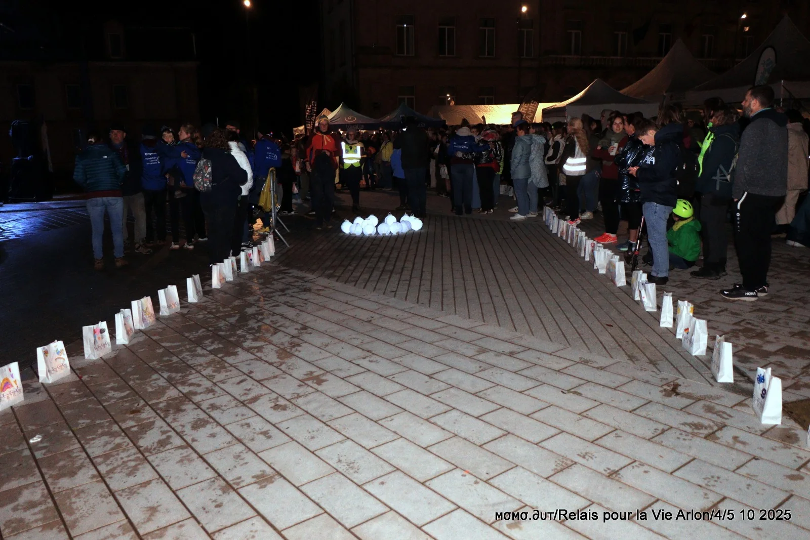 Des sacs-bougies alignés au sol la nuit sur la place Léopold, participants en arrière-plan, cérémonie des bougies du Relais pour la Vie d’Arlon