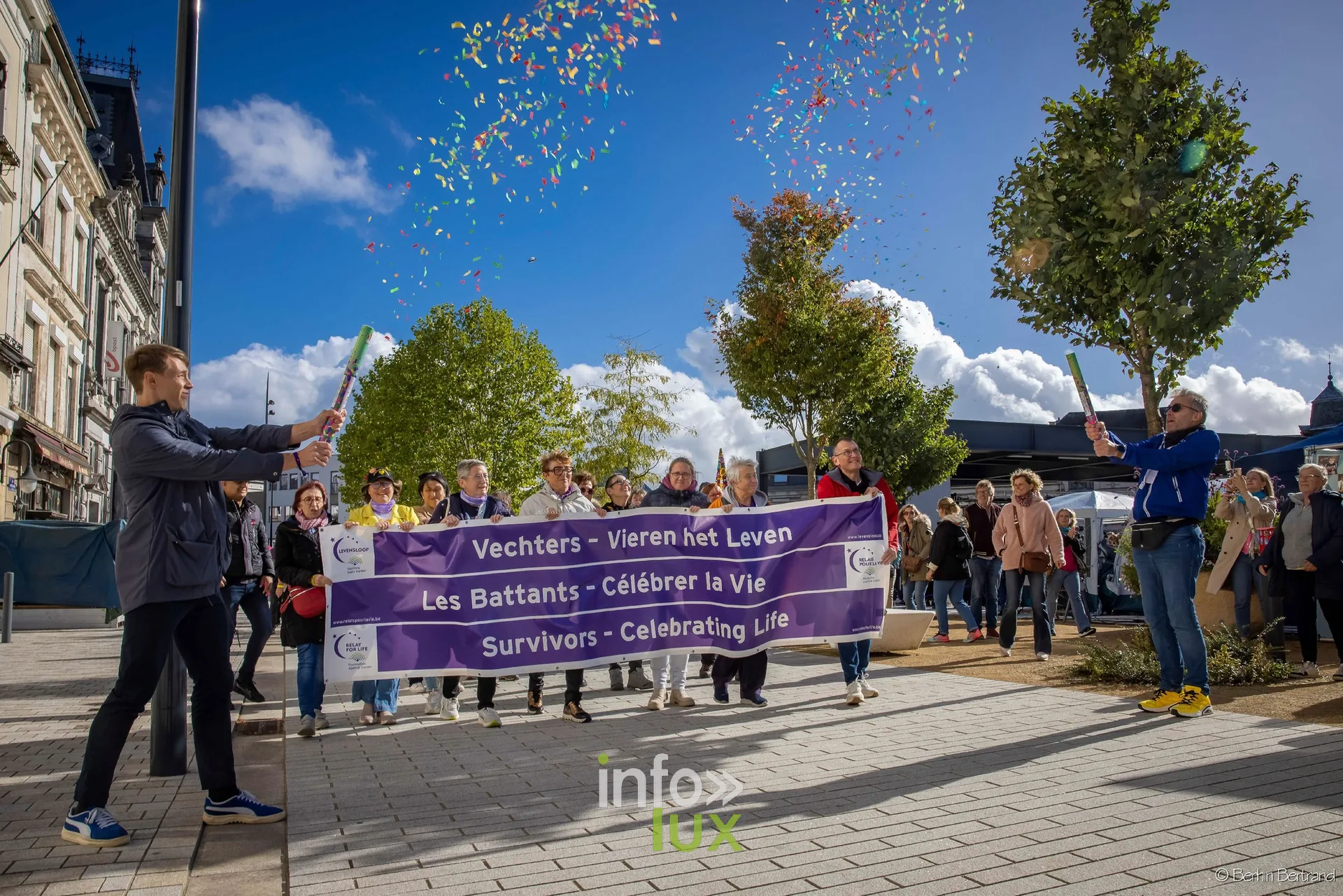 Des participants tiennent la bannière « Les Battants – Célébrer la Vie » sous une pluie de confettis, place Léopold à Arlon