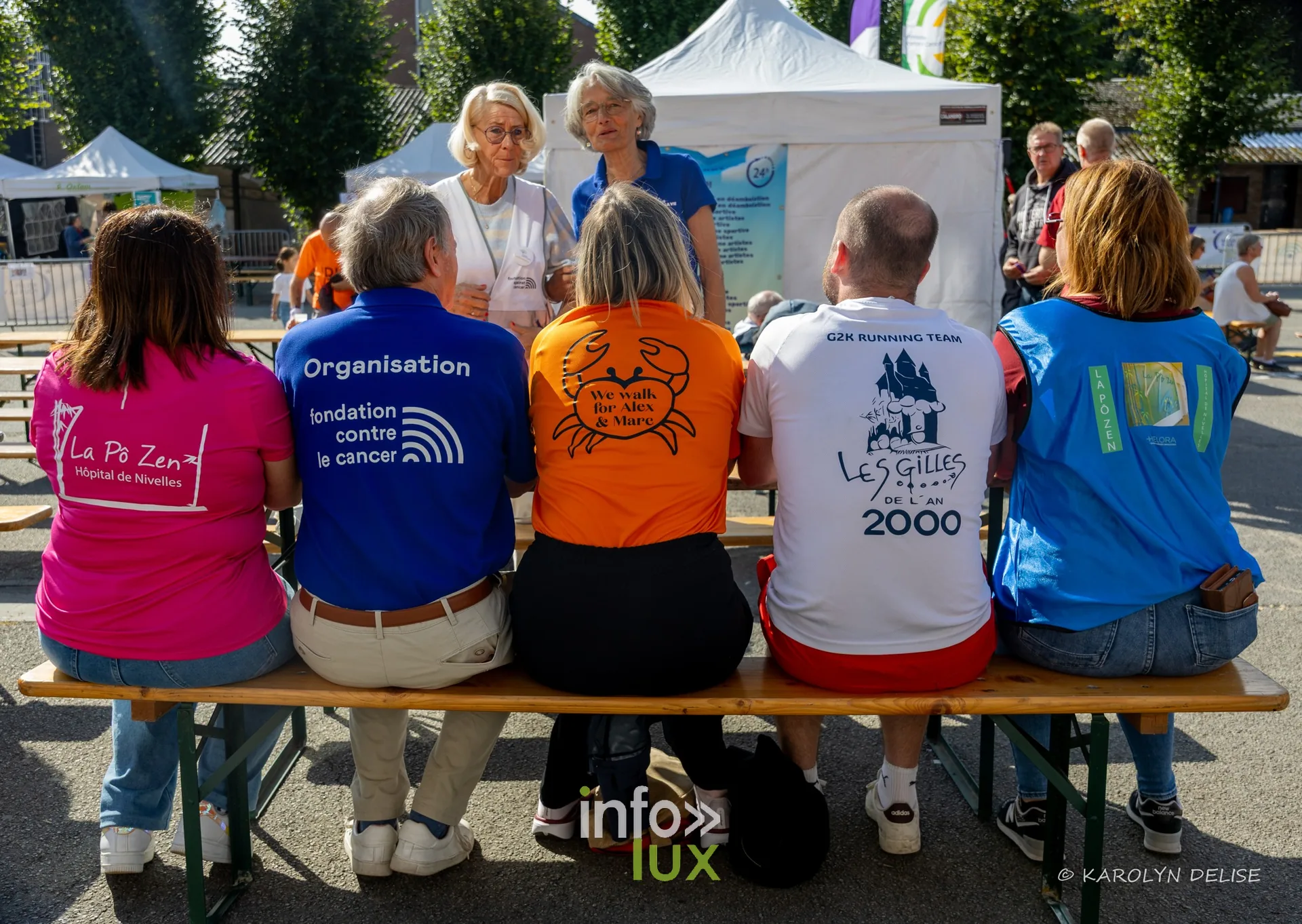 Participants de plusieurs équipes assis sur un banc, vus de dos, Relais pour la Vie de Nivelles 2026