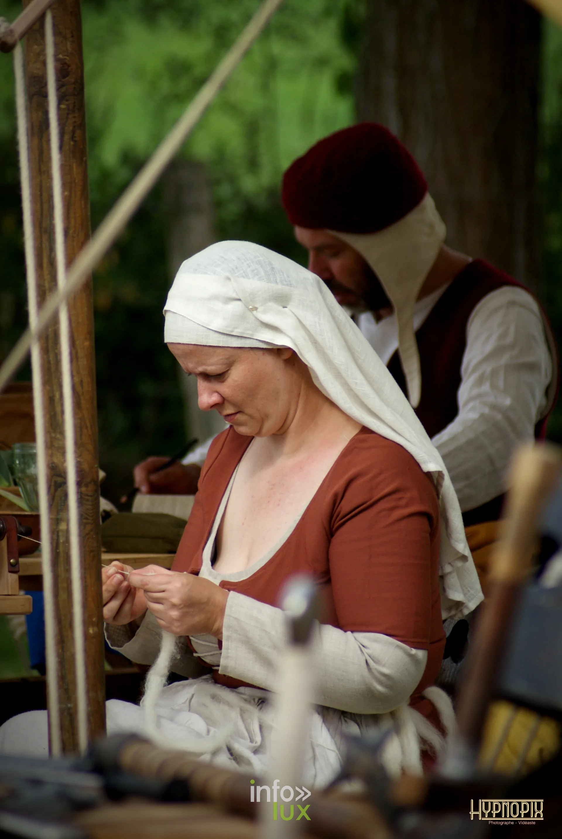 Femme en costume médiéval assise au campement, les mains à l’ouvrage, à Braine-le-Château