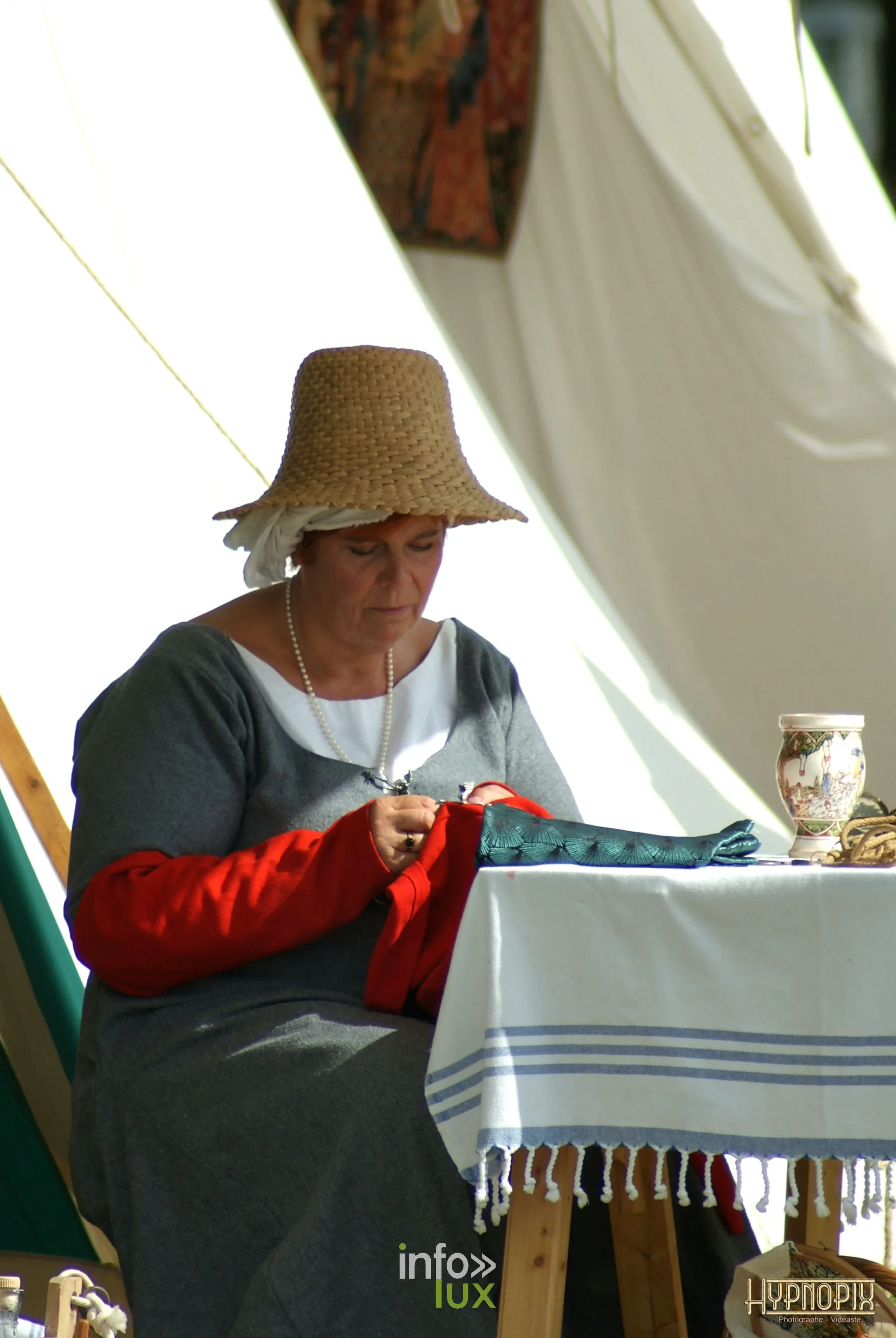 Femme au chapeau de paille cousant sous une tente aux Rencontres Médiévales de Braine-le-Château