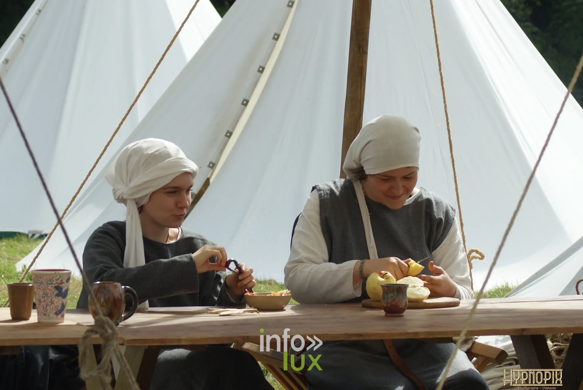 Deux femmes en costume médiéval épluchant des légumes à une table du campement de Braine-le-Château