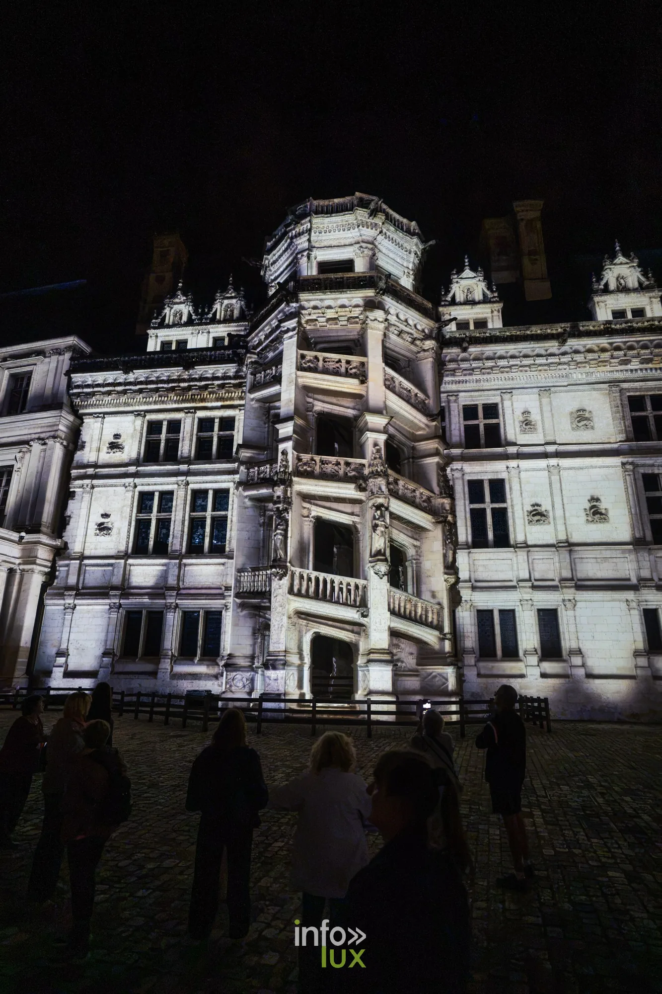 Façade Renaissance du château de Blois éclairée en blanc, spectateurs debout dans la cour