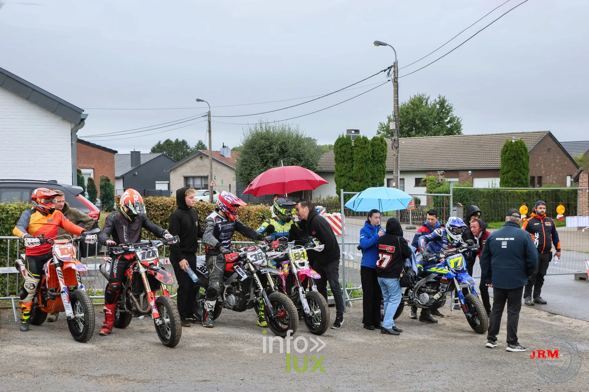 Supermotard de Battice 2026, Herve (province de Liège) : pilotes et accompagnateurs en pré-grille, sous quelques parapluies