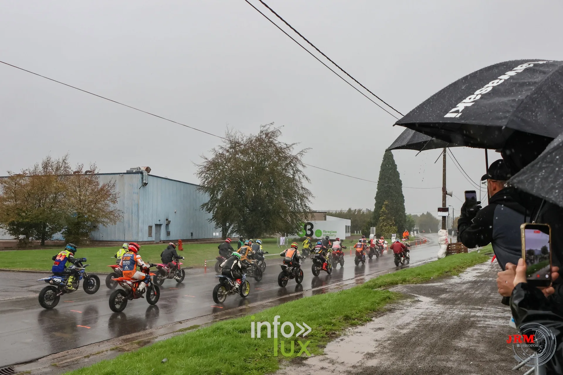 Supermotard de Battice 2026, Herve (province de Liège) : file de pilotes sur la route détrempée, public sous les parapluies