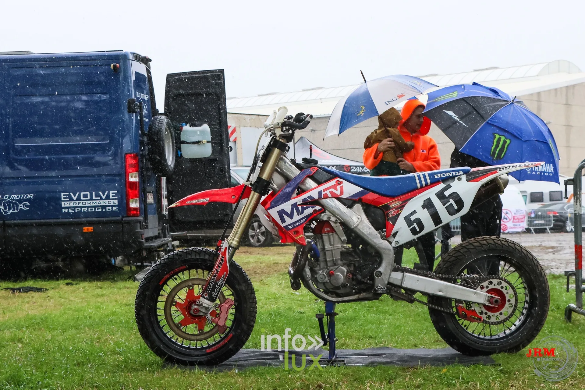 Supermotard de Battice 2026, Herve (province de Liège) : moto n°515 sur béquille dans le paddock, propriétaires sous les parapluies