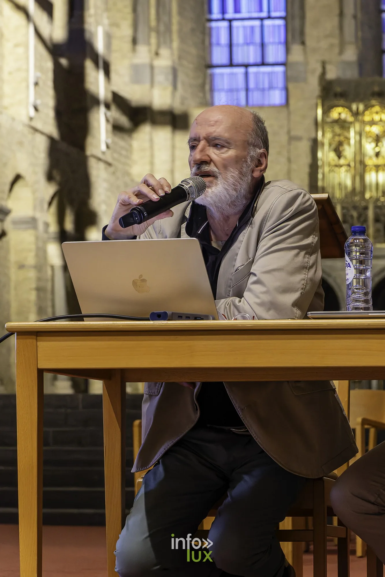 Un intervenant assis à la table présente les images projetées, ordinateur devant lui