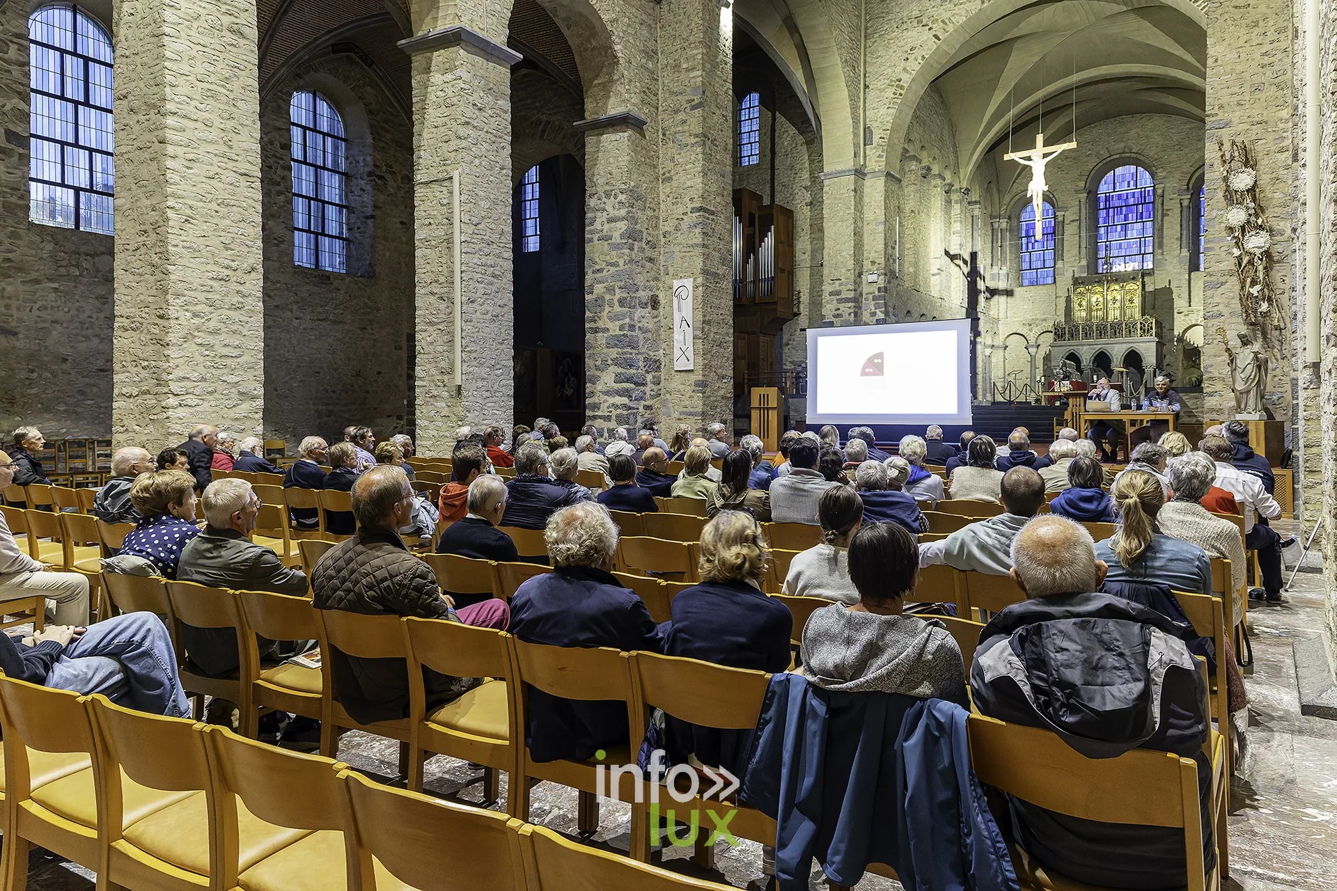 Vue depuis les bancs : l’écran de projection dans le chœur, le public au premier plan