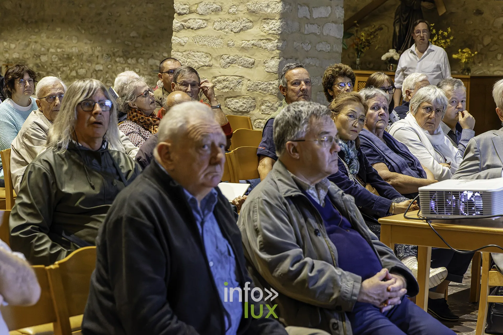 Un homme en veste sombre, bras croisés, écoute avec attention