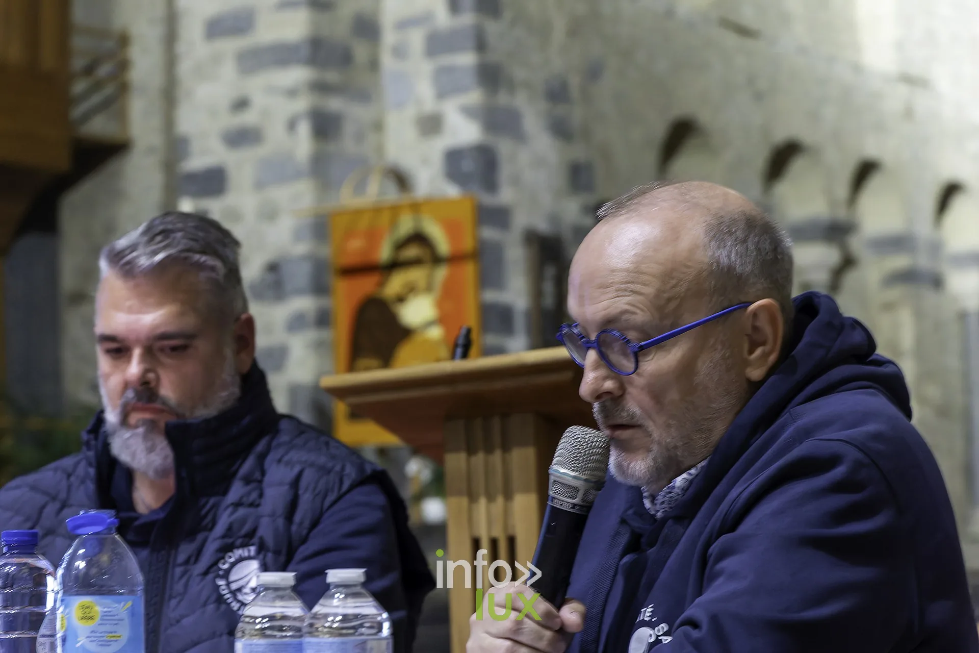 Deux hommes à la table des intervenants, micro et bouteilles d’eau