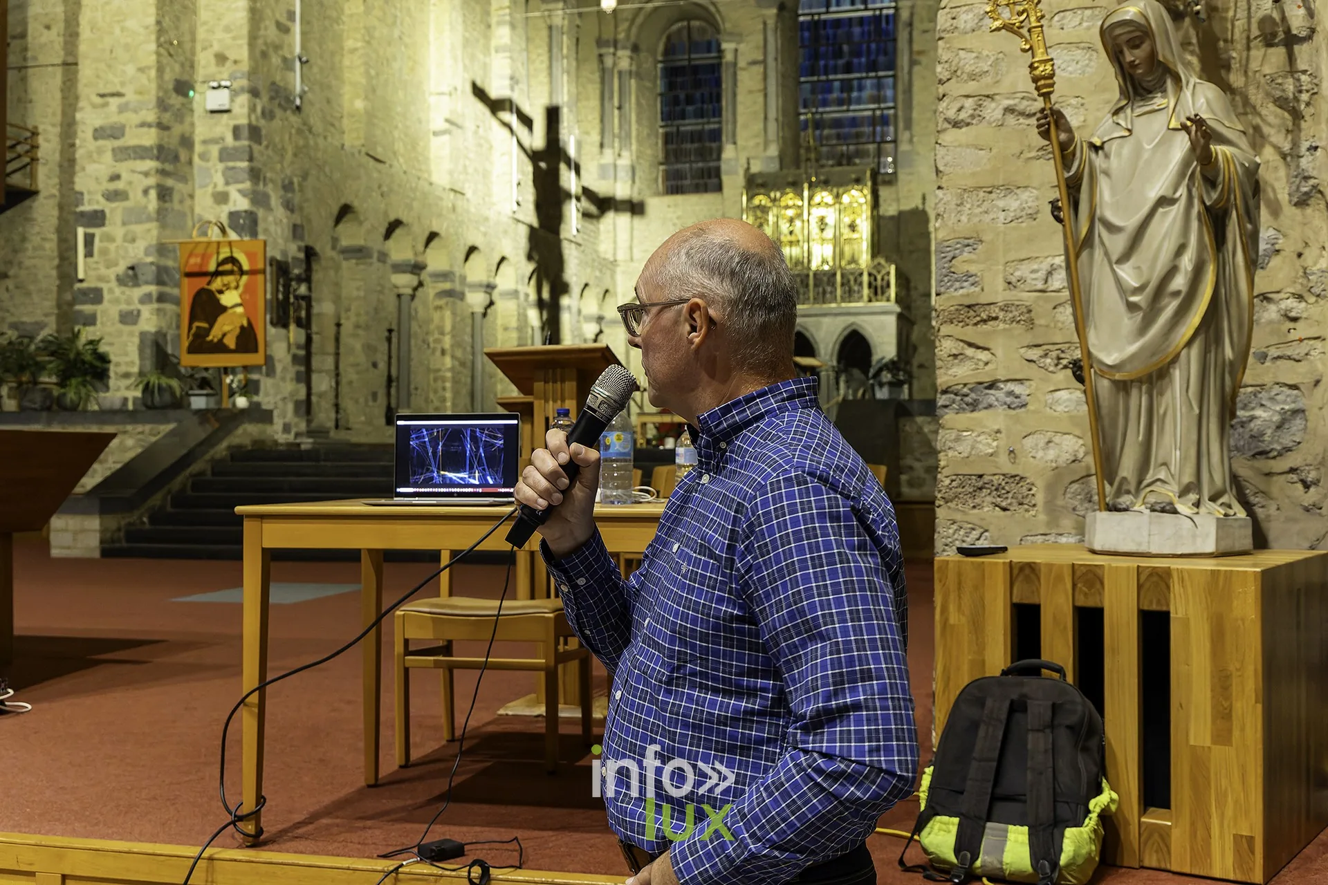 Un intervenant au pupitre, micro en main, devant une statue et le crucifix