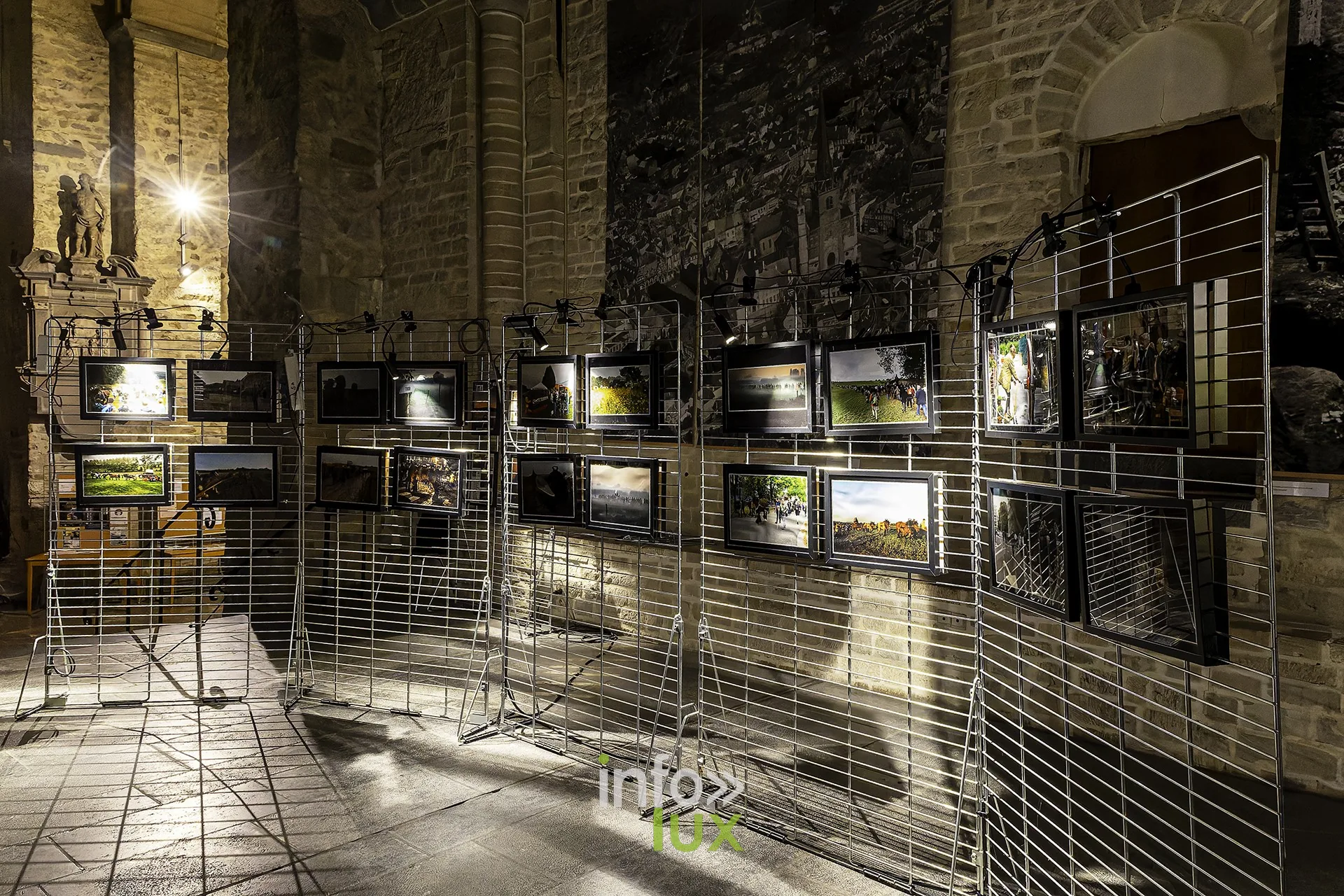 Visiteurs découvrant l’exposition photo sur grilles dans le chœur de la collégiale, en contre-jour