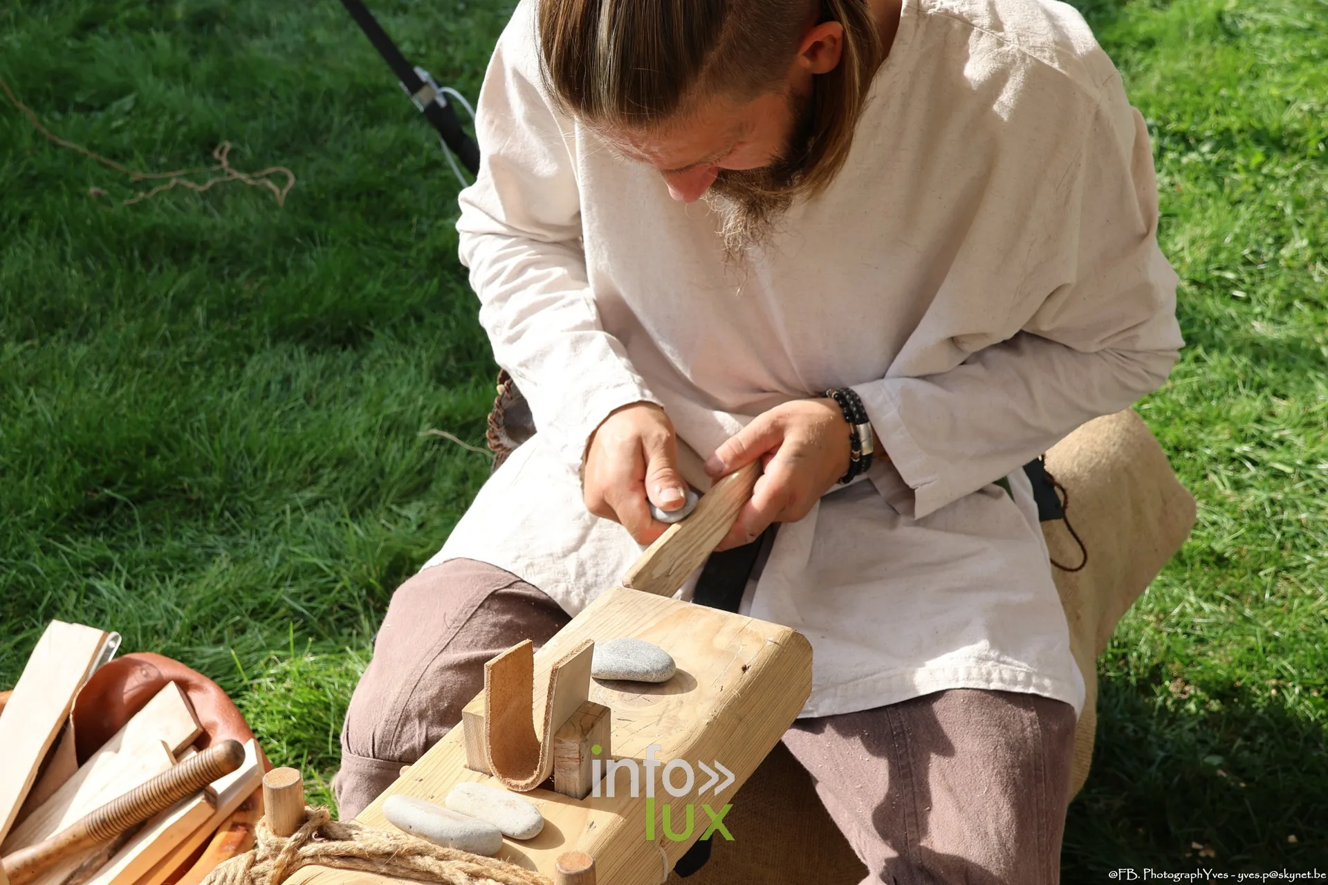 Artisan en chemise de lin taillant une pièce de bois, campement des Valhalla Days 2026