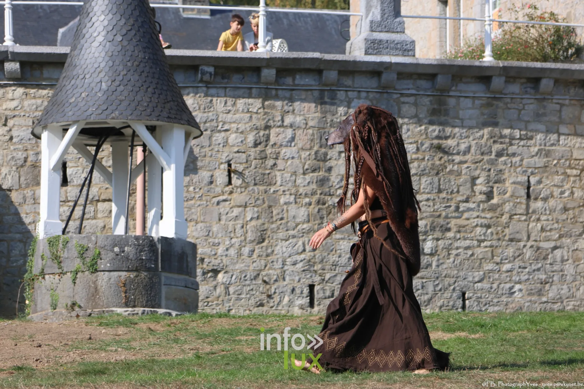 Personnage en robe de bure devant le mur d’enceinte du parc Saint-Roch à Ciney