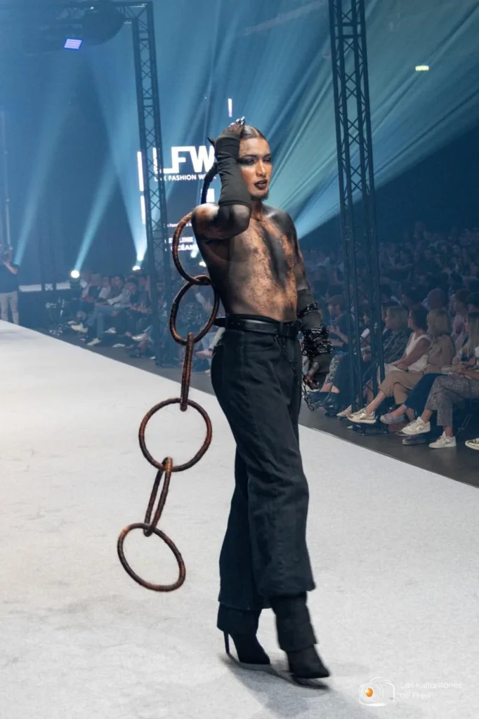 Youness sur le podium de la Lux Fashion Week 2026, chaîne d’anneaux en cheveux à la main, devant le public, Arlon