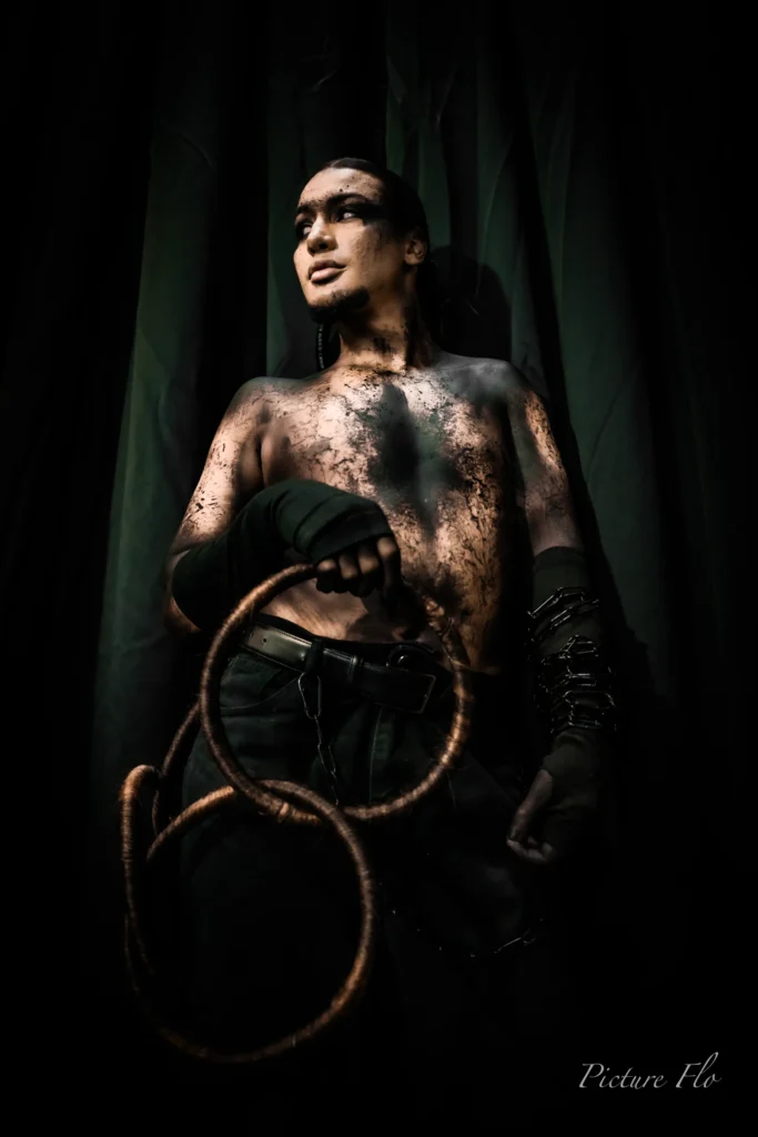Youness en coulisses devant le rideau, anneaux en cheveux en main, torse maquillé de noir craquelé, Lux Fashion Week 2026, Arlon