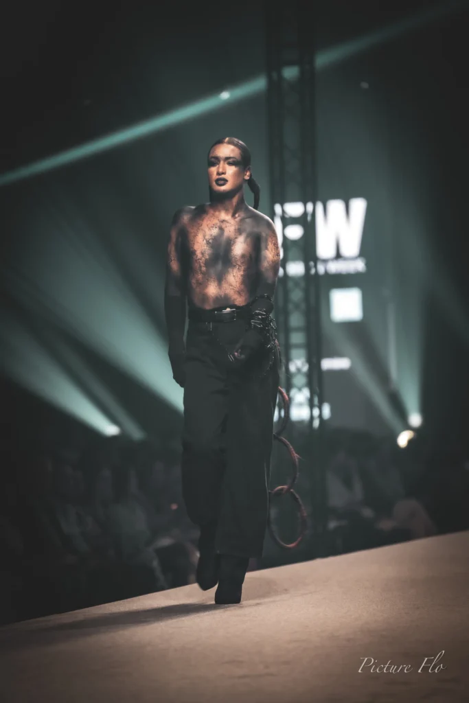 Youness avance sur le podium devant l’écran LFW, gants noirs et pantalon large, Lux Fashion Week 2026, Arlon