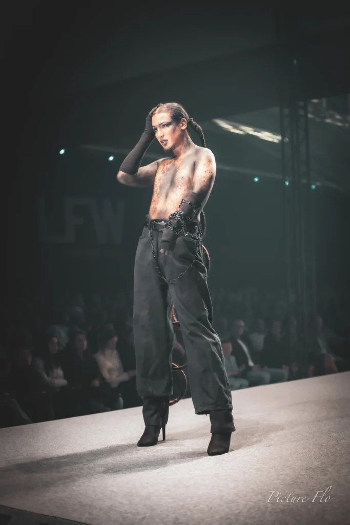 Youness sur le podium, main dans les cheveux, chaîne d’anneaux le long de la jambe, Lux Fashion Week 2026, Arlon