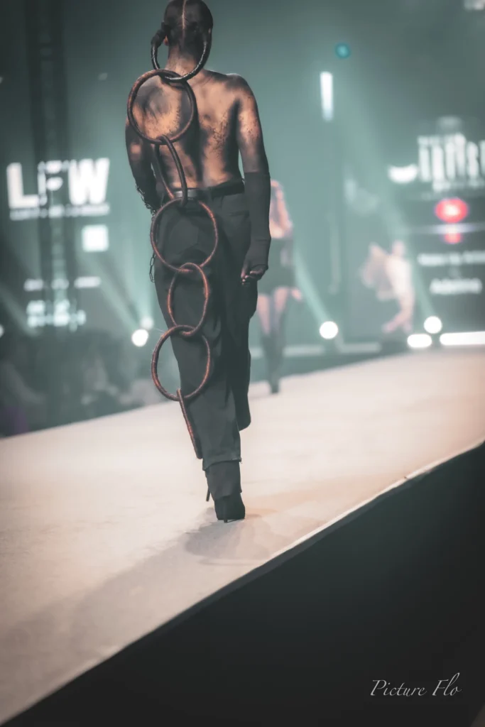 Youness de dos en fin de podium, anneaux en cheveux, devant l’écran LFW, Lux Fashion Week 2026, Arlon