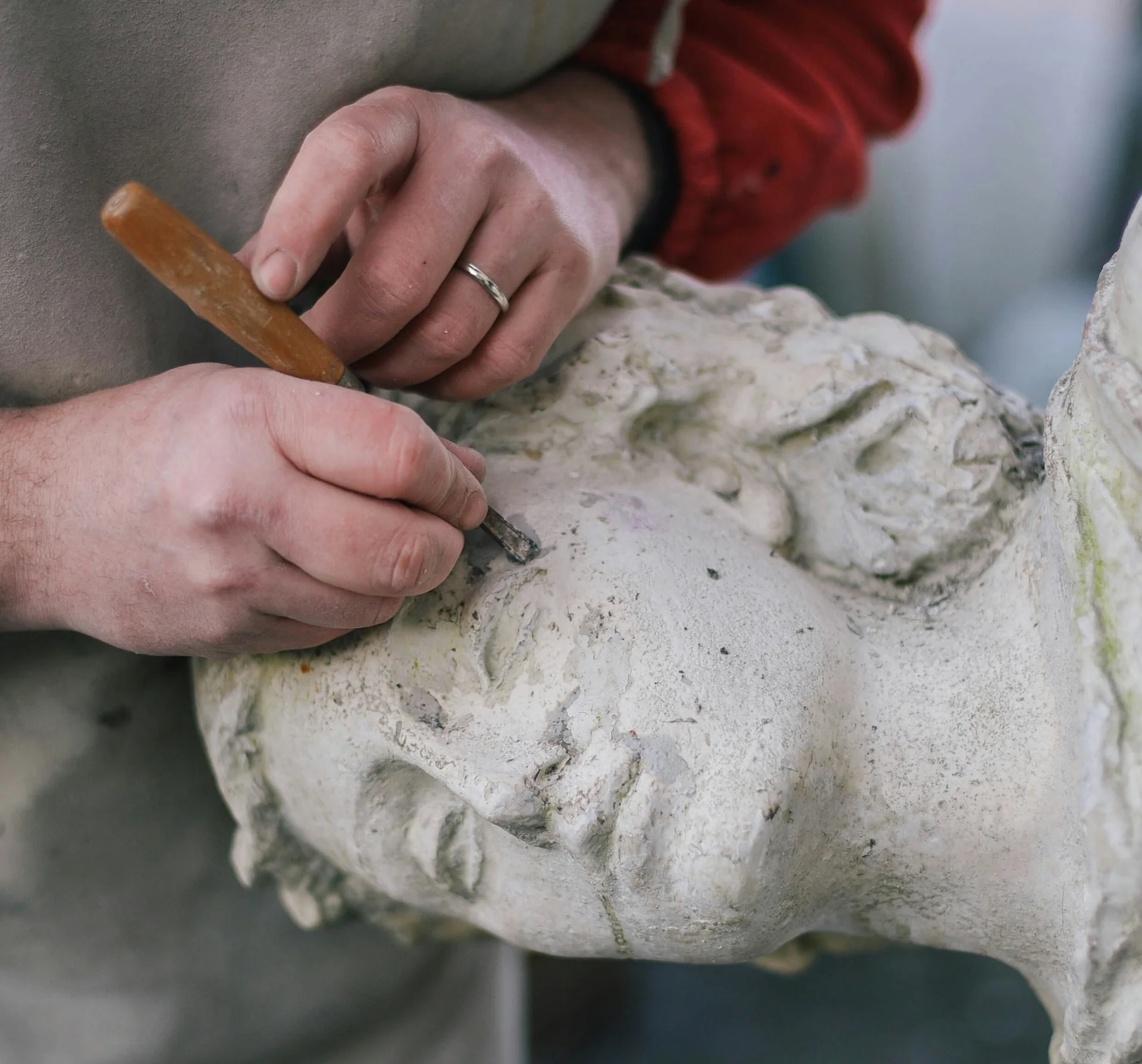 Des mains travaillent au ciseau une tête de statue sculptée