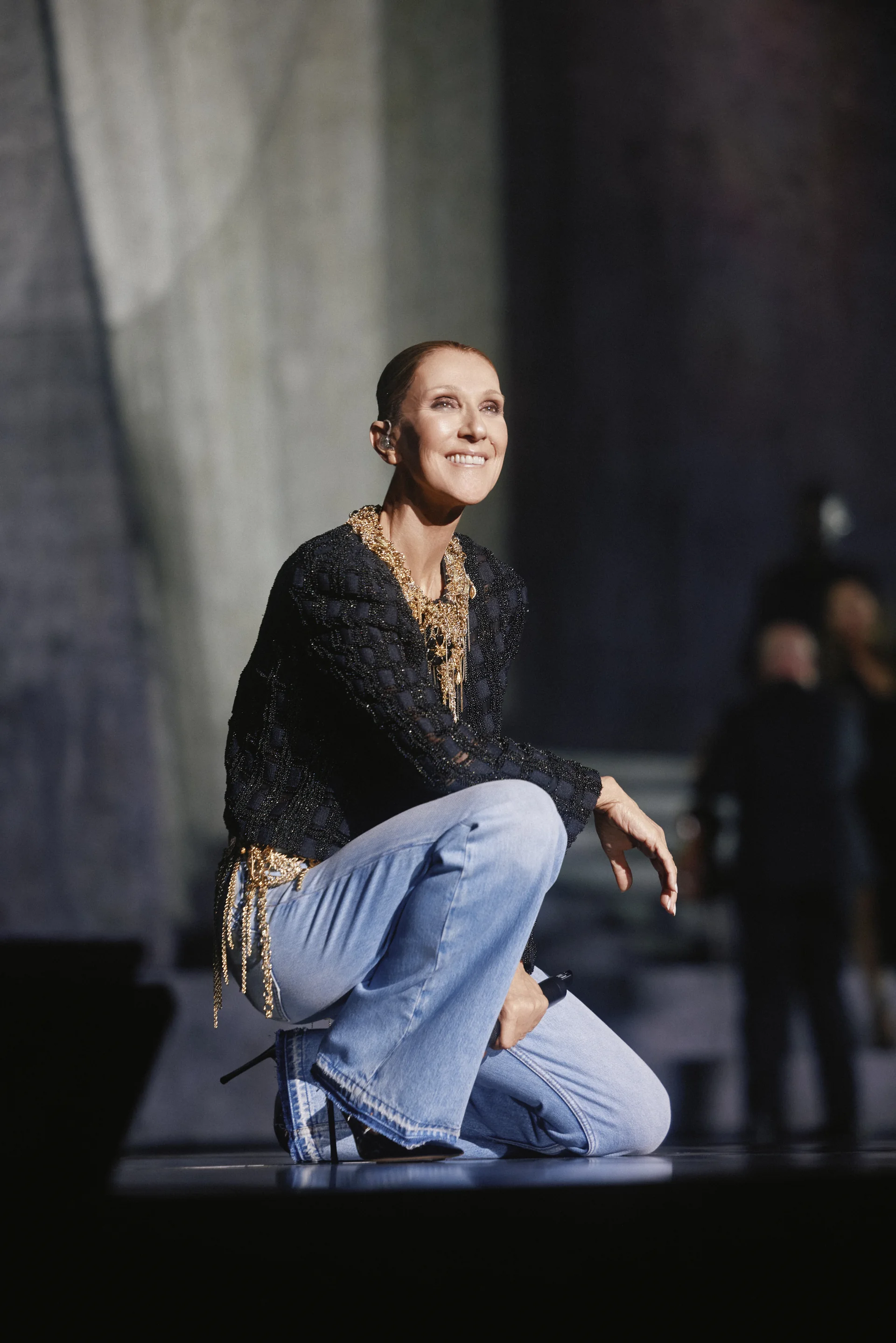 Céline Dion agenouillée, le regard levé vers le public de la Plenitude Arena