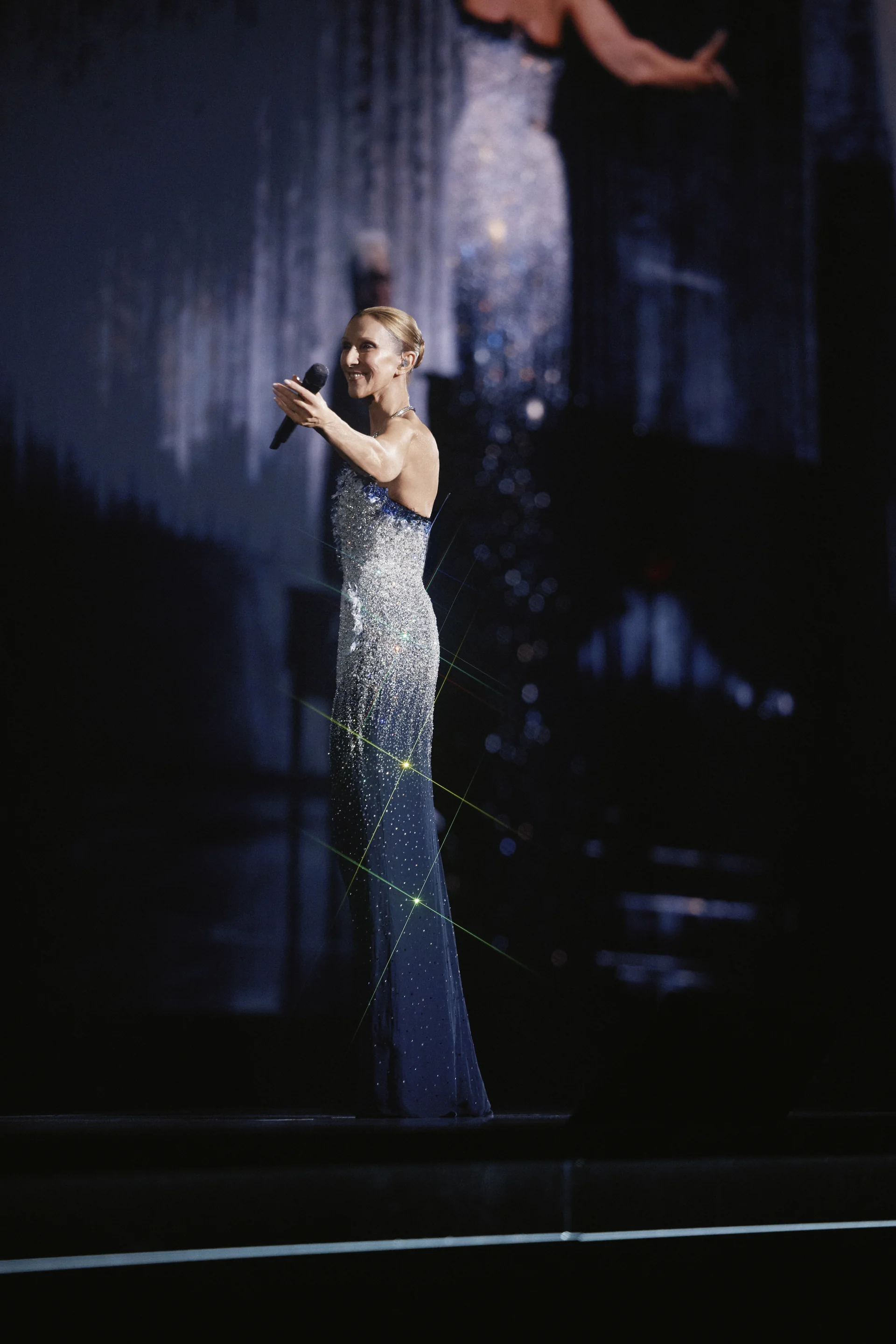 Céline Dion en robe longue brodée de cristaux, micro en main, à la Plenitude Arena