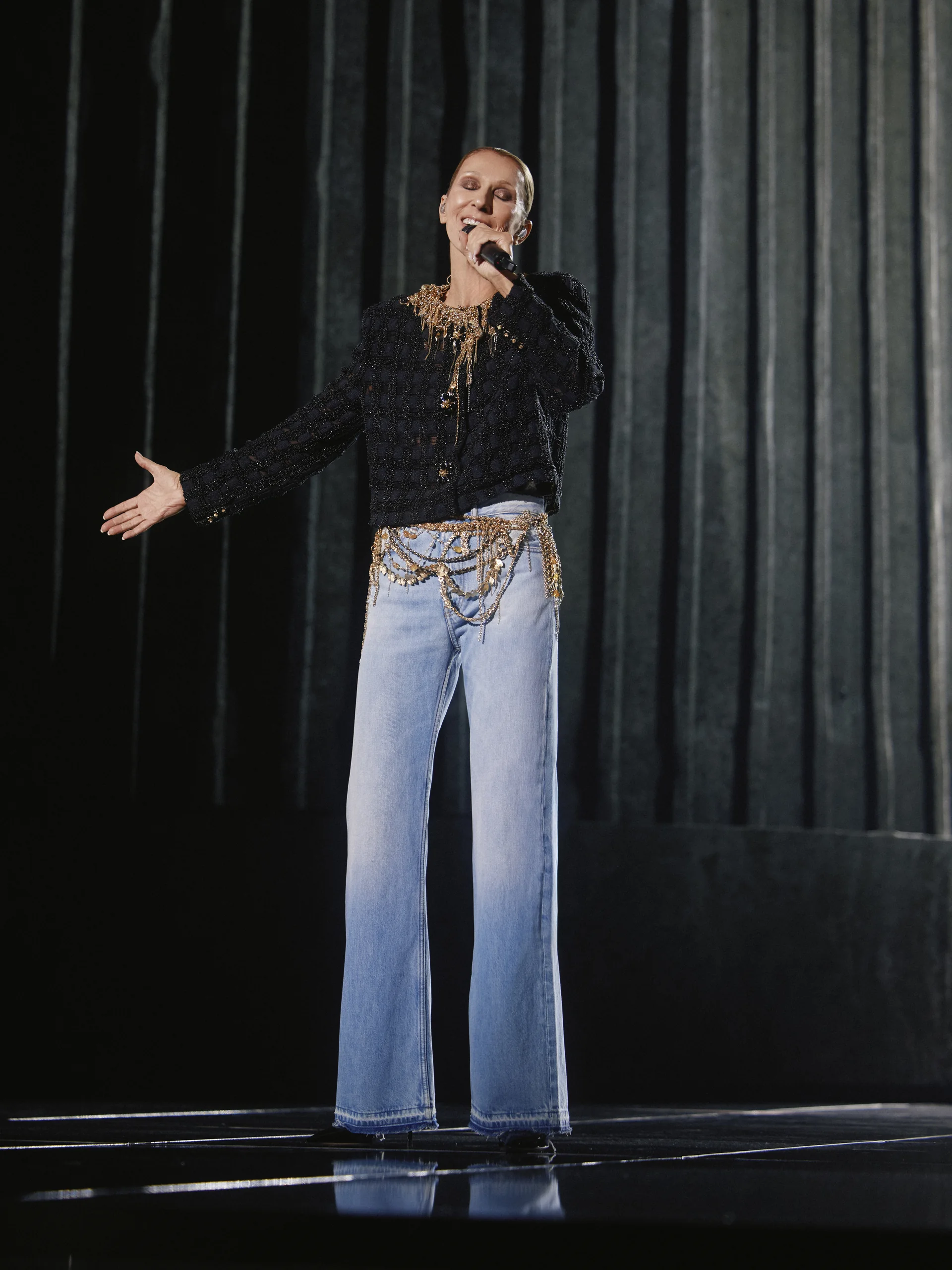 Céline Dion en veste noire et jean, micro en main, à la Plenitude Arena