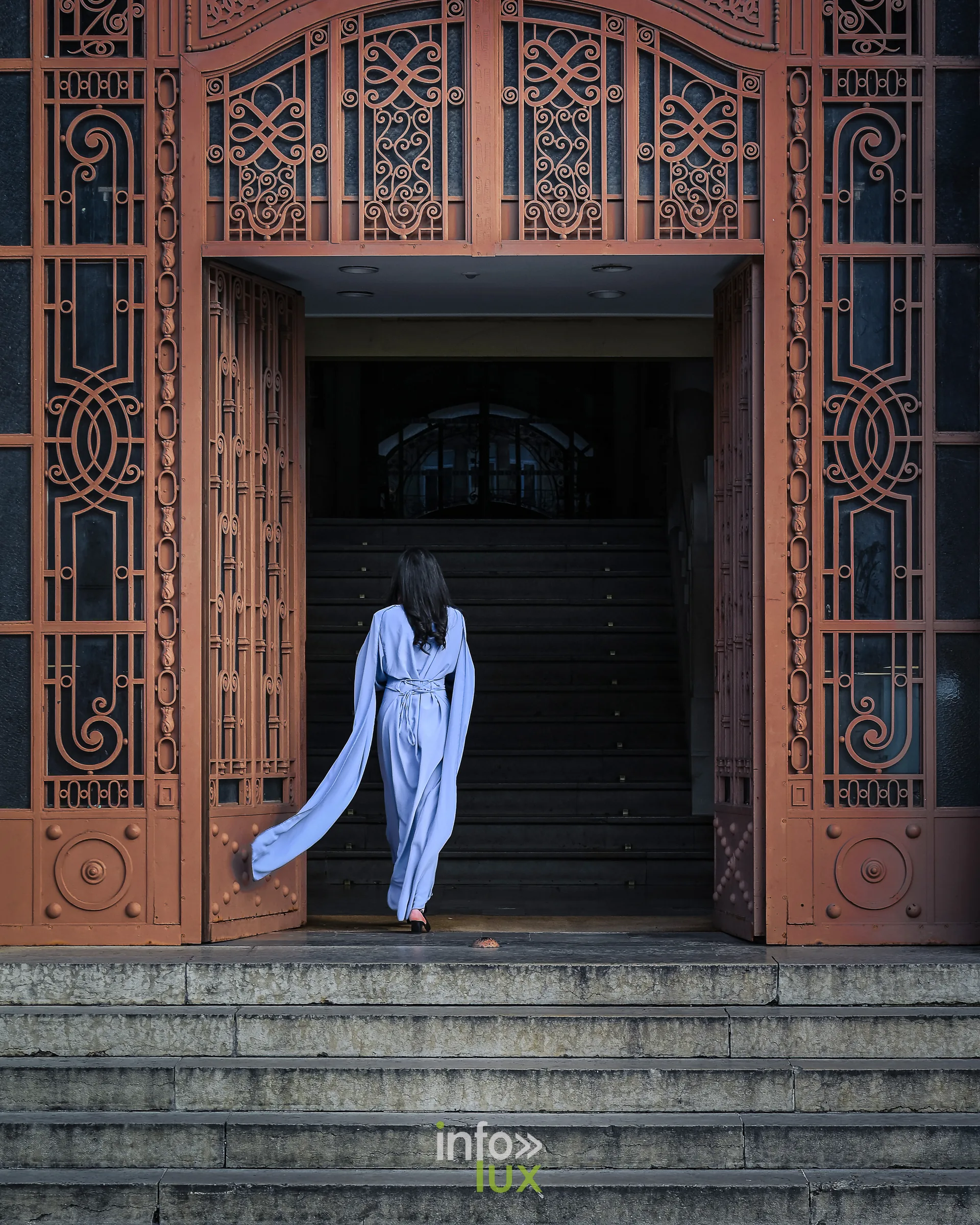 Femme en robe bleue franchissant une porte en fer forgé, photo Dolorès Photographie