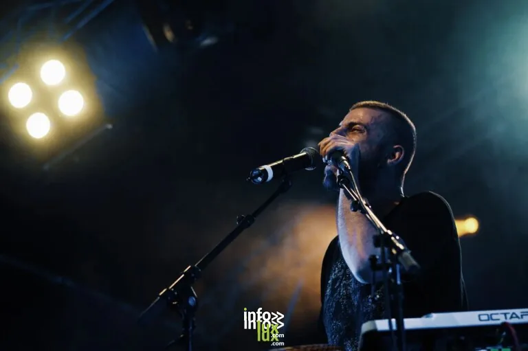 Une performance dynamique en concert live d'un chanteur masculin avec un groupe sous les lumières vives de la scène.