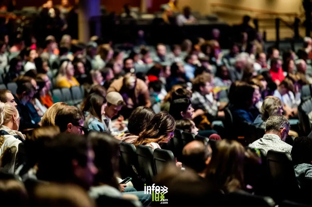 Une foule diversifiée assise dans un auditorium, engagée dans un événement en intérieur.