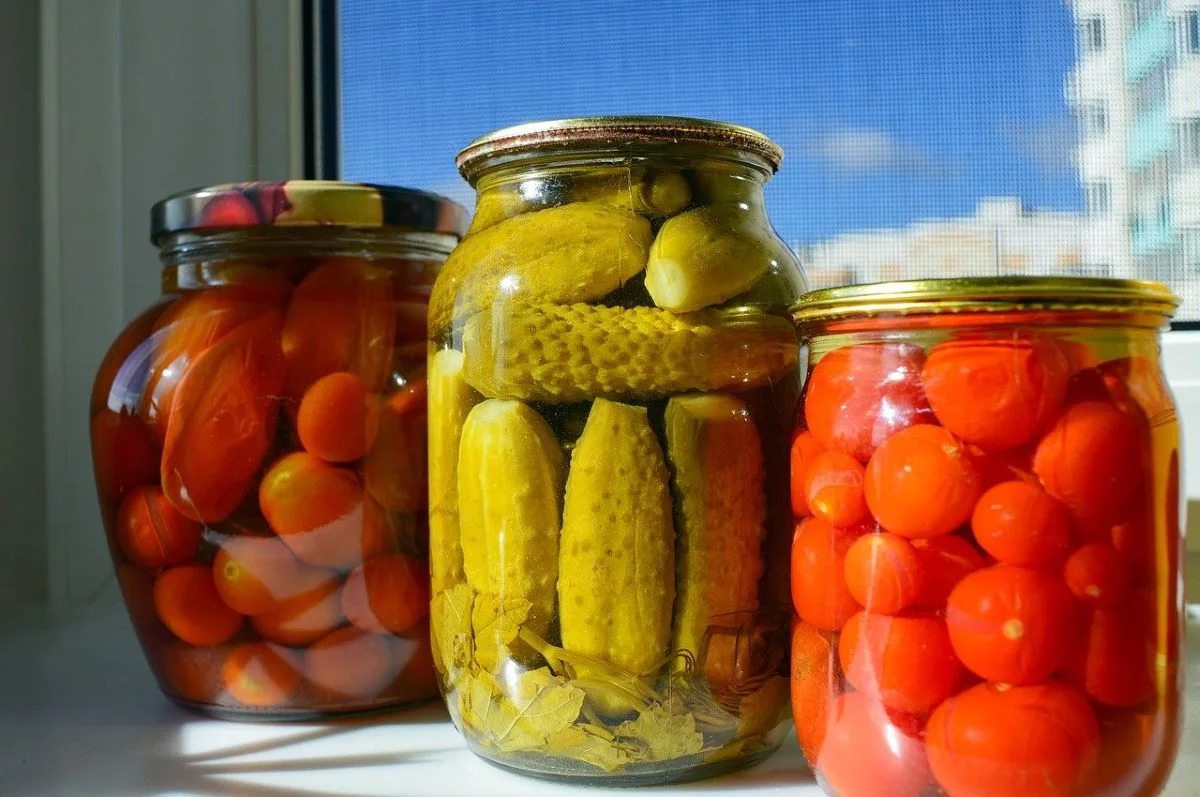 Trois bocaux de légumes conservés : tomates cerises et cornichons
