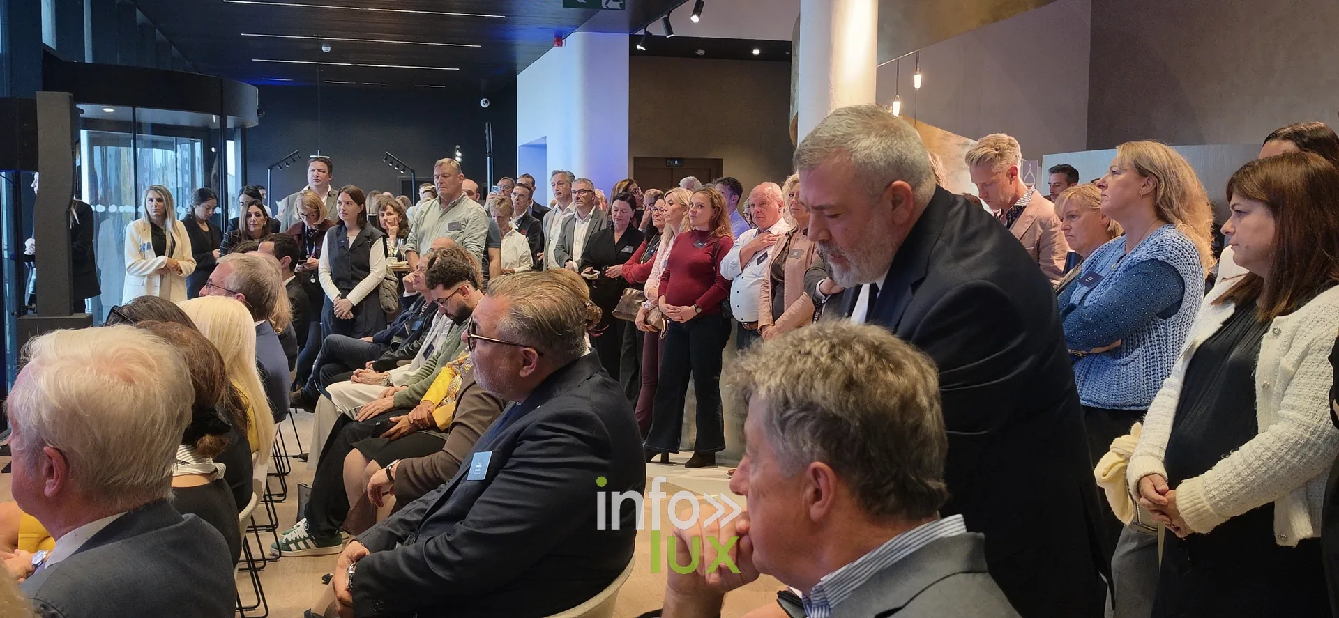 Des invités debout au fond de la salle, inauguration du nouveau site Leonidas à Nivelles, 15 octobre 2026 (photo Karolyn Delisé-Hanse) — photo modifiée par ia