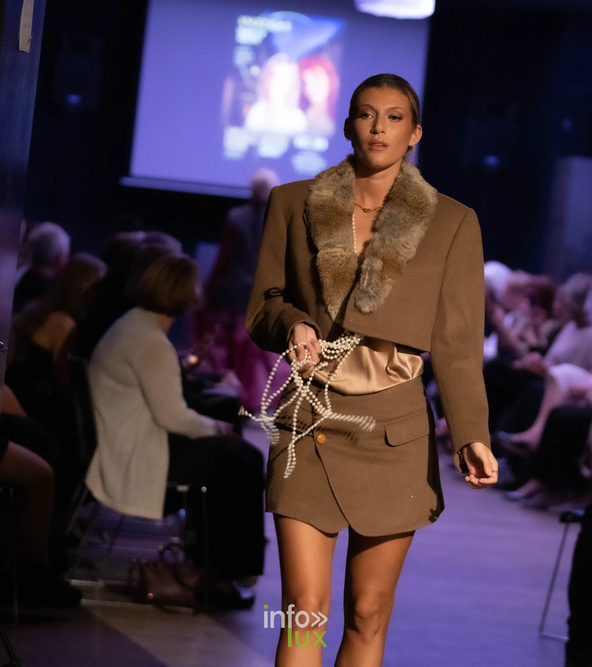 Liège Fashion Week 2026 au Musée Grand Curtius à Liège : mannequin en veste marron à col de fourrure et colliers de perles