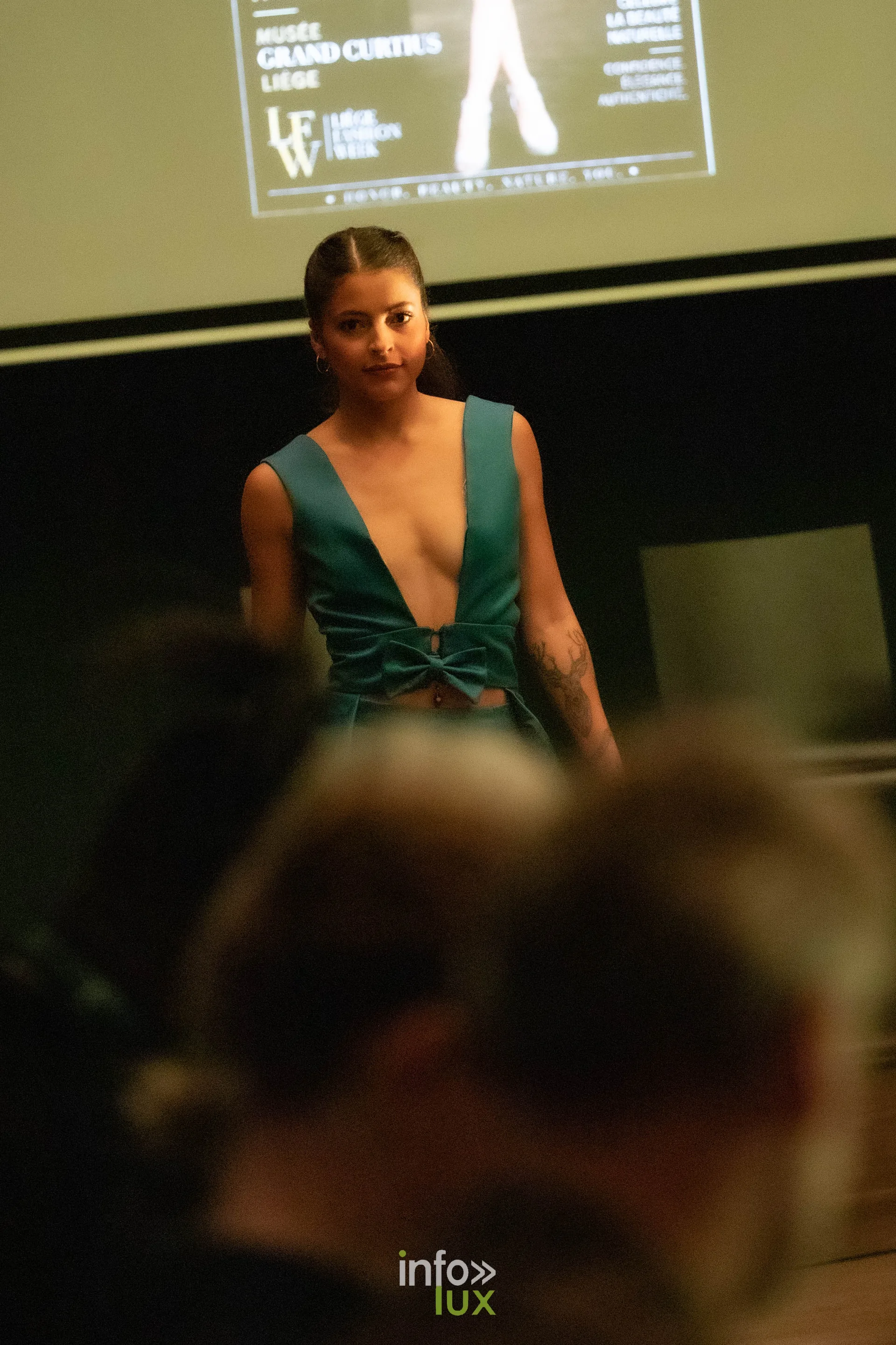 Liège Fashion Week 2026 au Musée Grand Curtius à Liège : mannequin en ensemble vert noué sous l’écran de la Liège Fashion Week