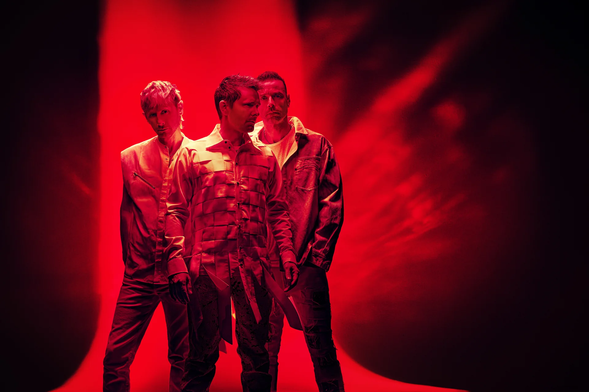 Les trois membres de Muse debout sous un halo de lumière rouge