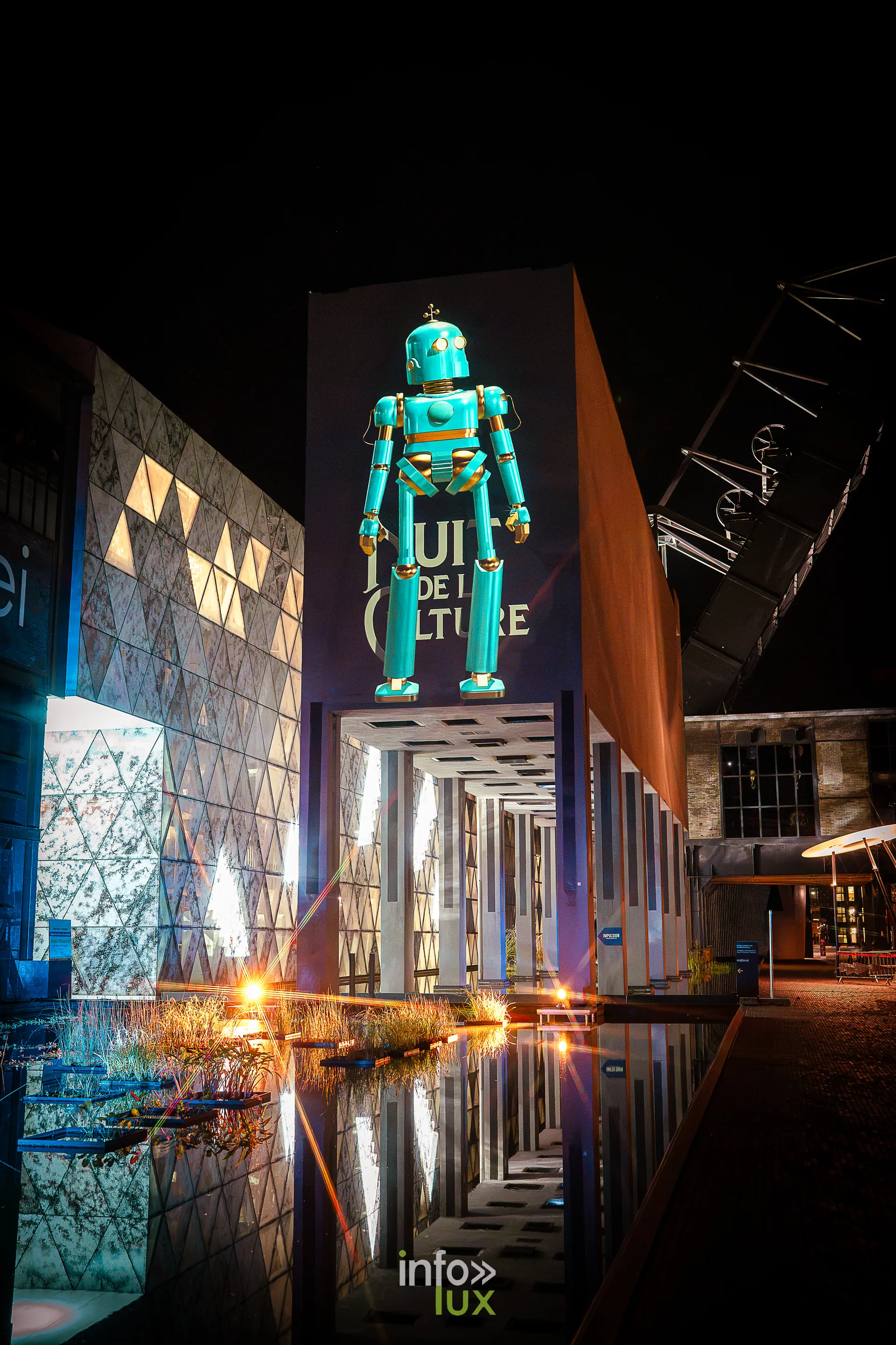 Nuit de la Culture 2026 à Esch-Belval : grand visuel du robot de la Nuit de la Culture sur une façade, reflété dans un bassin