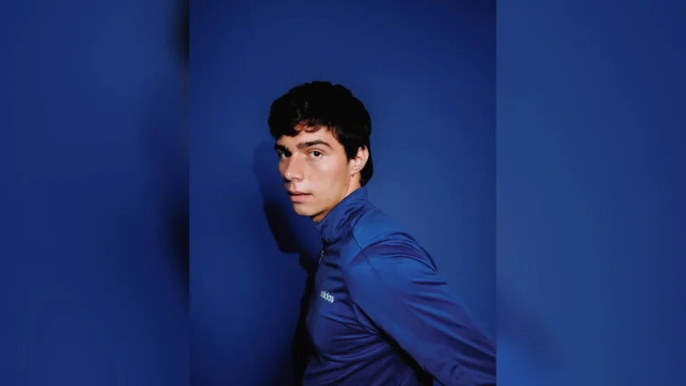 Portrait du rappeur Paolo., veste de survêtement bleue, devant un mur bleu