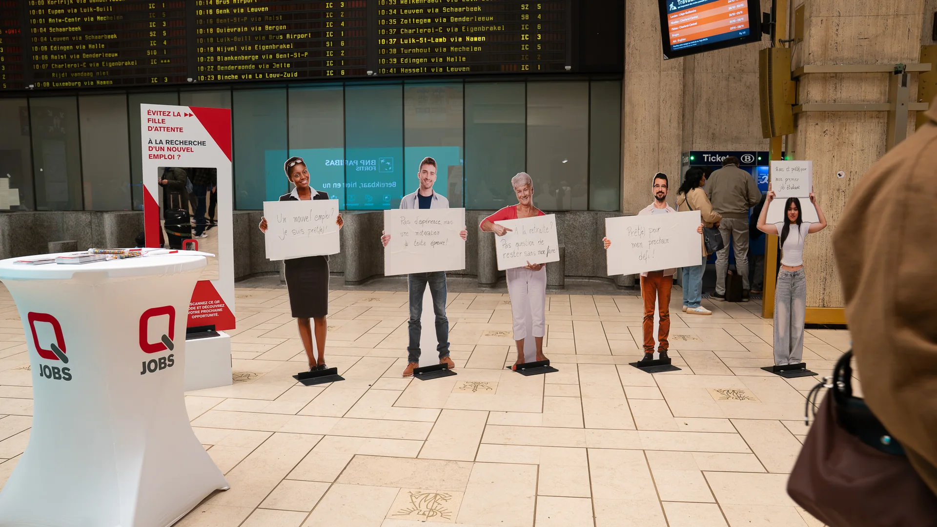Cinq personnages grandeur nature font la file devant la colonne-miroir de Q Jobs