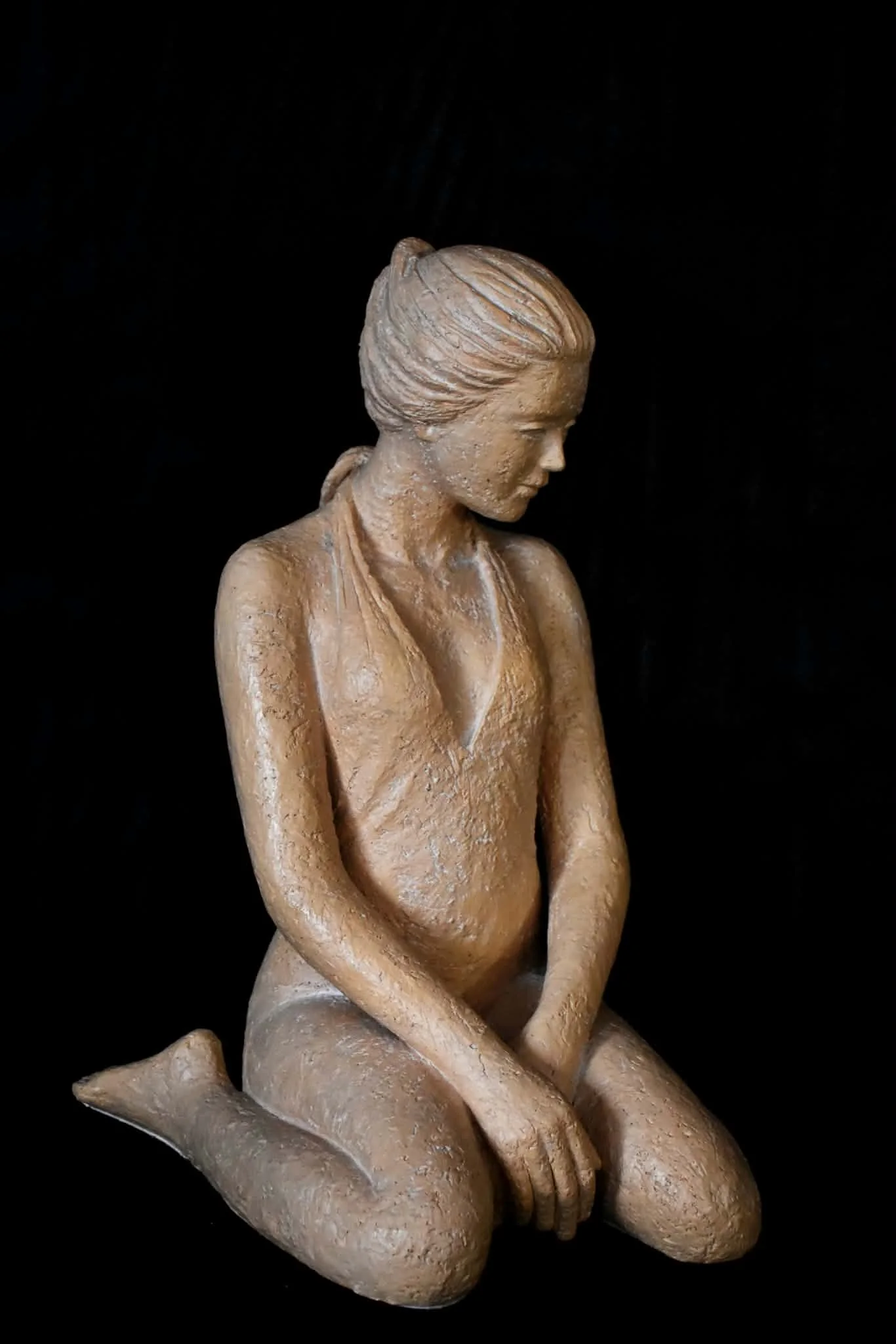 Sculpture d’une femme agenouillée, mains sur les genoux, sur fond noir