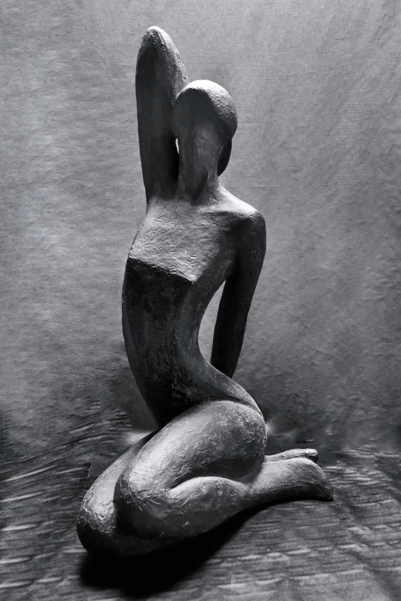 Sculpture d’une femme agenouillée, une main levée, en terre grise