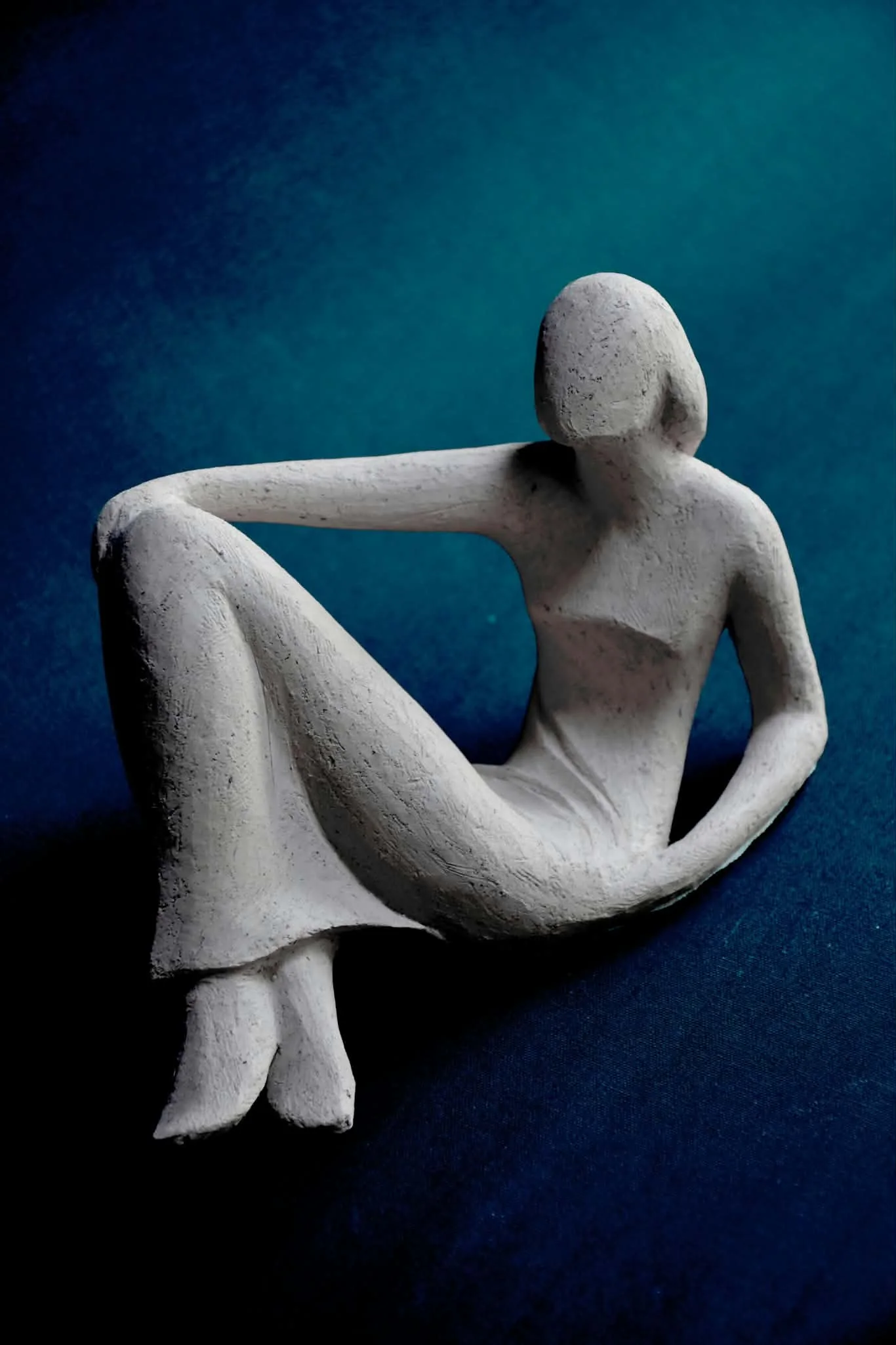 Sculpture épurée d’une femme assise, genou relevé, sur fond bleu